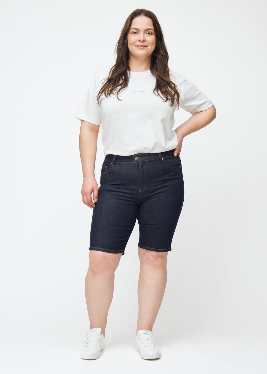 Plus-size model viser dyb mørkeblå denim shorts til kvinder i farven Midnights med skinny pasform i bevægelse.