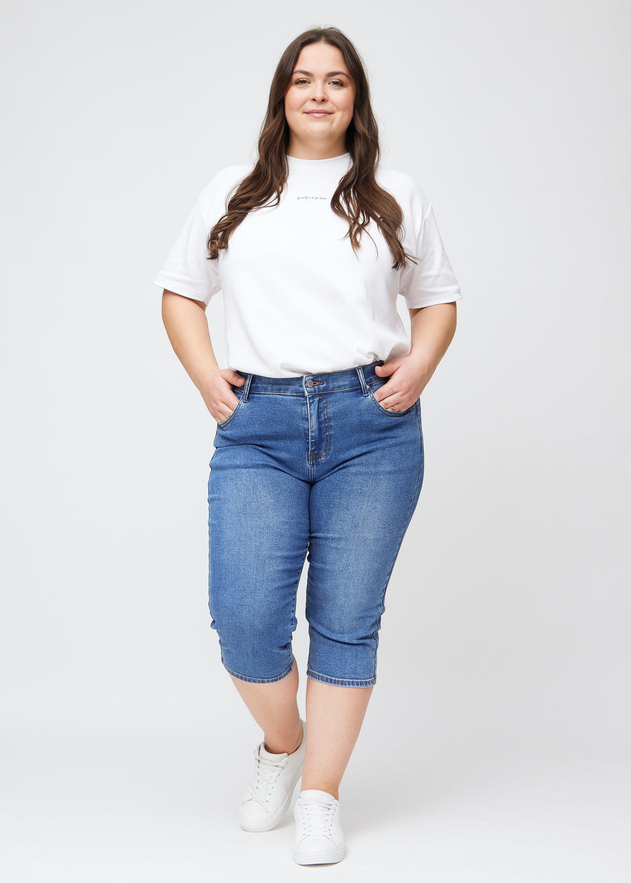 Plus-size model går ind i billedet, strækker i sine blå denim slim capris, drejer rundt for at vise dem frem og forlader derefter billedet.